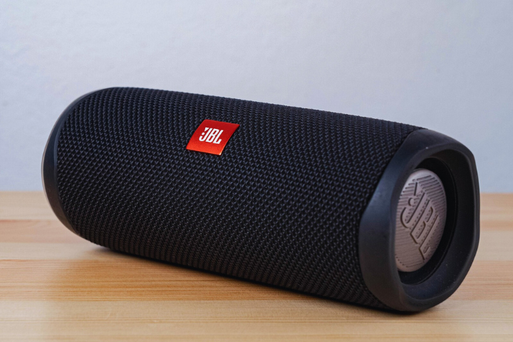A black JBL portable Bluetooth speaker with a mesh exterior is resting on a light wooden surface against a plain background.
