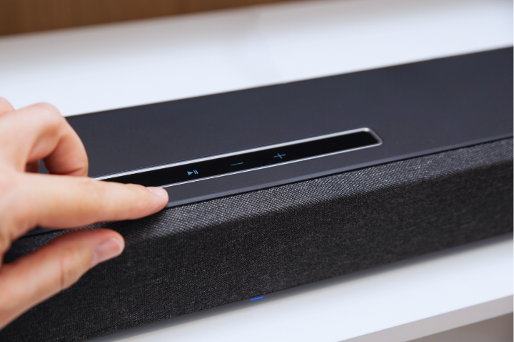 A hand presses the touch-sensitive play button on a sleek black soundbar