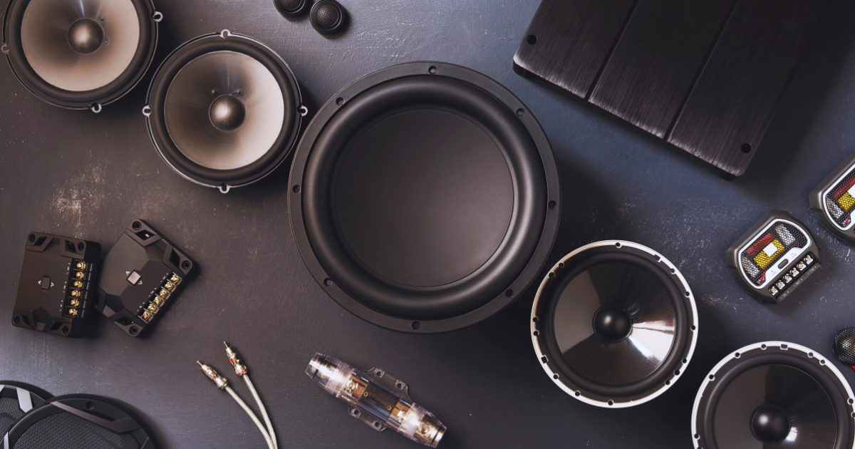Flat lay of audio equipment on a dark surface, featuring various speakers, capacitors, and cables.