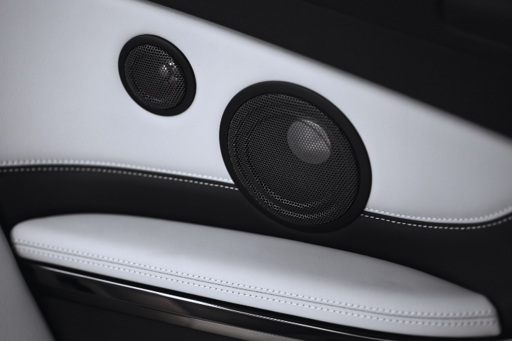 Close-up view of a car's interior door panel with two circular speakers on sleek white leather with black accents.