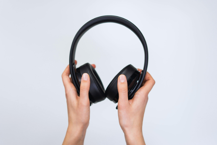 Two hands hold black over-ear headphones against a plain white background.