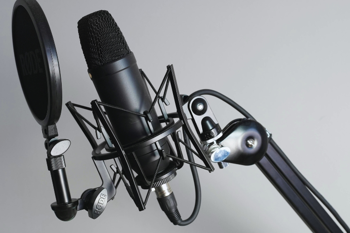 Close-up of a black studio microphone with a pop filter on an adjustable boom arm, set against a grey background.
