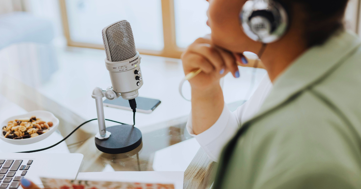 glass table with a microphone A person wearing headphones sits at a glass table with a microphone, laptop, and a bowl of nuts.